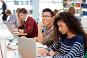 Group of students smiling and talking in front of a computer.