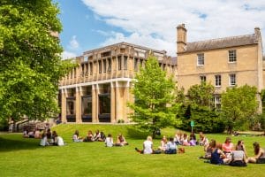 Front view of an Oxford University building with several students sitting on the grass communing with each other