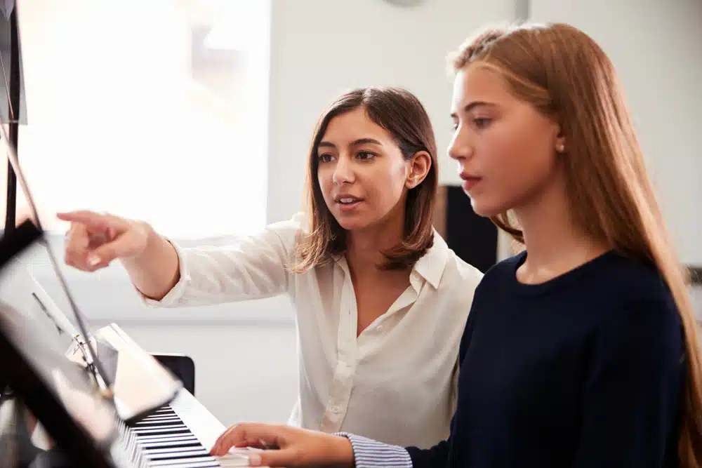 a female piano teacher helping her student learn how to play the piano