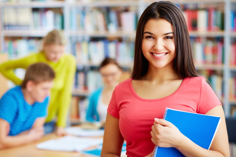 Female student smiling at the camera while holding a book.