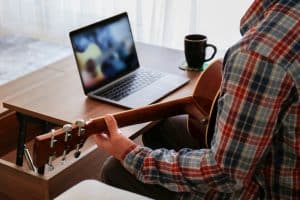 View of a student playing a guitar in front of his laptop.