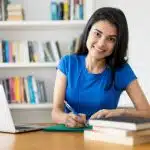A young woman studies at a desk with books and a laptop, symbolizing the choice between Northeastern vs UC San Diego.