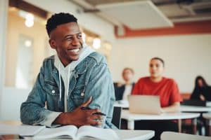 a male student sitting inside a classroom and smiling