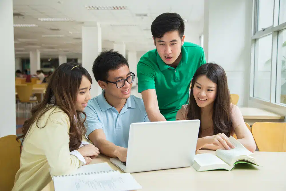 Asian students talking in front of a laptop.