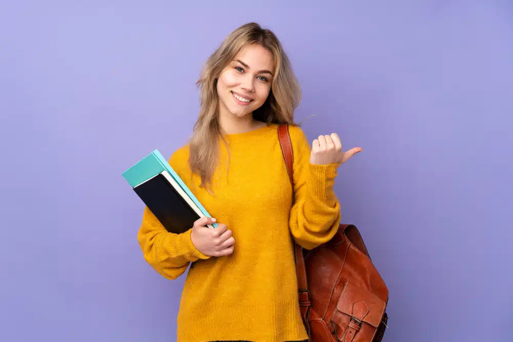 a female student carrying her bag and notebooks while looking at the camera smiling