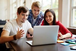 Three students talking in front of a laptop.