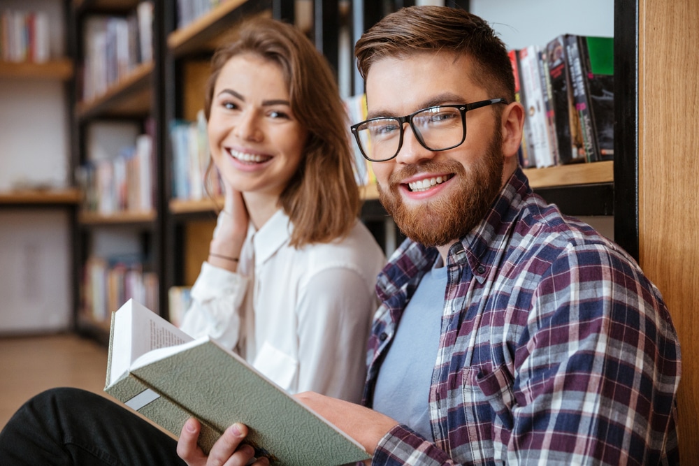 two college students inside a library and smiling while looking at the camera