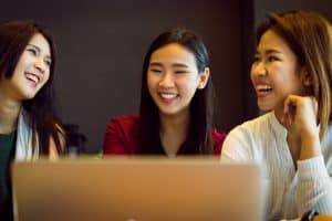 Group of female students laughing and talking in front of a laptop.