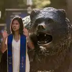 an UCLA student posing beside a bear statue, the inspiration behind the UCLA official mascot
