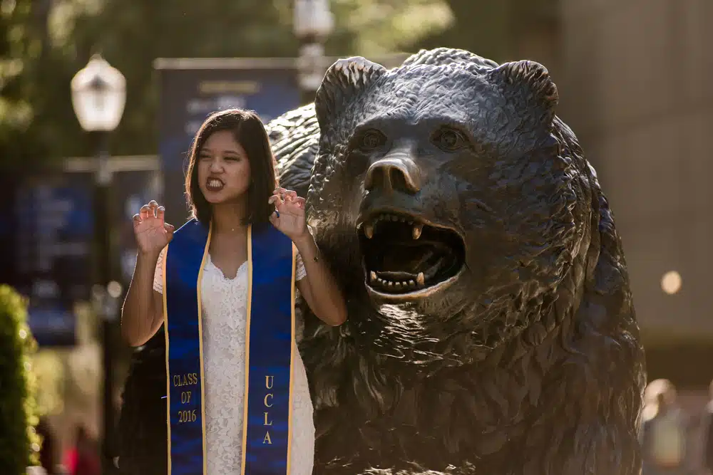 an UCLA student posing beside a bear statue, the inspiration behind the UCLA official mascot
