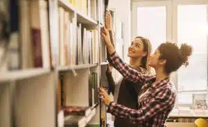 a female student grabbing a book from a library shelf