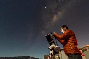 a male astronomer looking at the night sky through his telescope