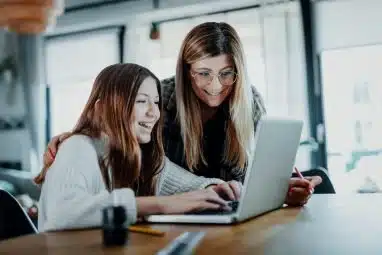 A mother and daughter smile while looking at a laptop together while researching Berkeley vs Yale.