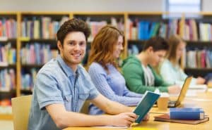 Male student holding a book in a library.