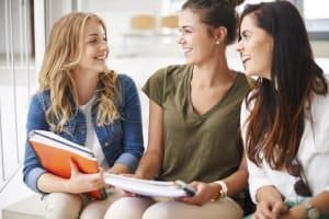 Three students talking while sitting on a bench.