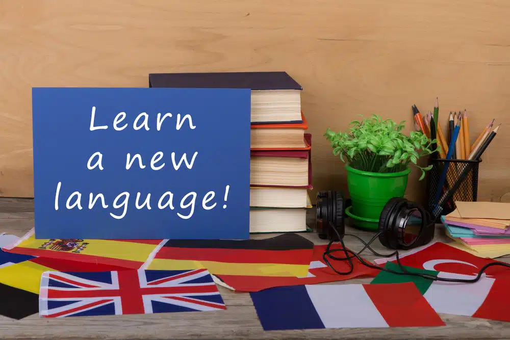 Sign with learn a new language placed on a table with different flags.