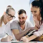 Three high school students collaborating on an essay outdoors, representing teamwork and analytical writing skills needed for the AFSA National High School Essay Contest