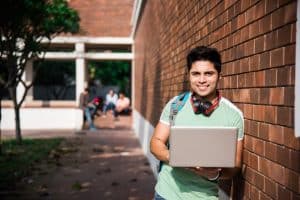 a male student carrying a laptop while standing