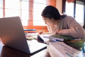 Young female student focused on her desk in the bedroom, studying at home with a laptop.