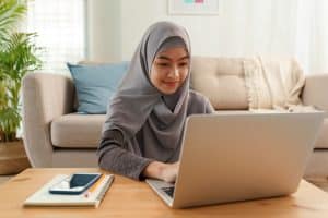 a young muslim woman wearing a hijab and typing unto her laptop