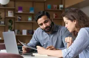 Indian male mentor and latin female young professional sitting in creative office space.