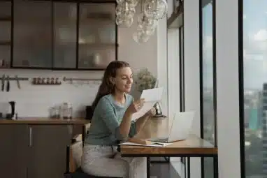 Happy young woman reading paper letter at home.