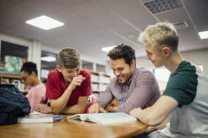 two male students reading with a teacher