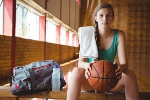 famle student inside a locker room and carrying a basketball