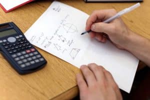 a person solving a math problem while a calculator is on the table