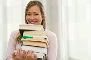 Smiling student holding a stack of books for high school research project.