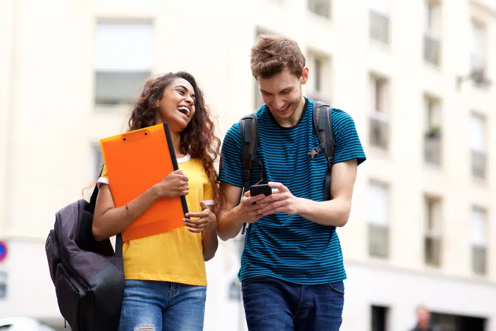 Portrait of happy students walking with bag and mobile phone