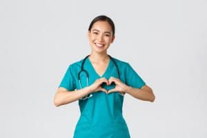 female nurse in scrubs showing heart gesture and smiling