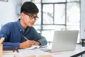 Young collage student using computer and mobile device studying online.