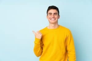 Male teenager isolated on sky blue background pointing to the side to present a product