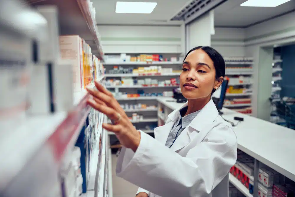 Young woman working in pharmacy looking for medicine in shelf standing behind counter