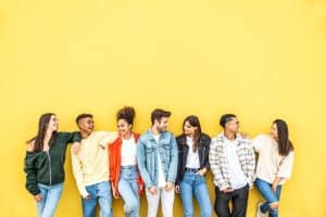 Diverse community of college students smiling together on a yellow wall background