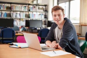 Male Student Working At Laptop In College Library