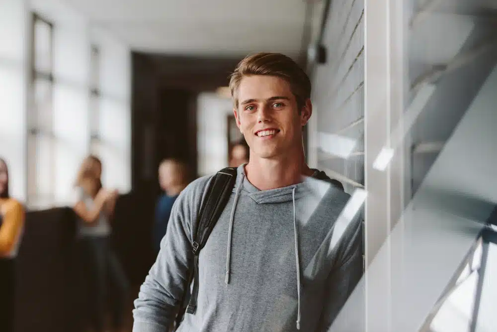 Portrait of teenage male student standing wall in corridor of a college.
