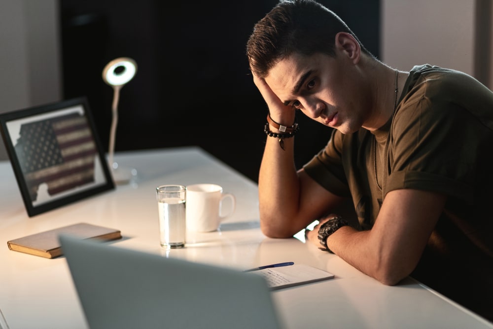 Sad student looking at his laptop in his dorm room.