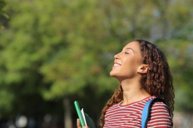 A young woman smiles while taking notes and studying on her laptop, possibly comparing USC vs Boston University.