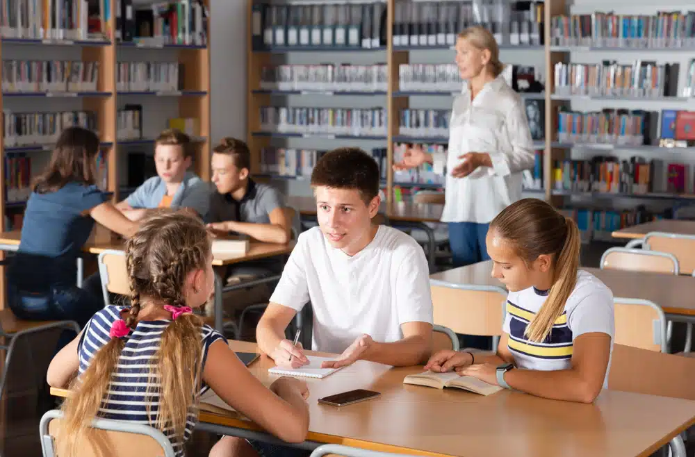 Attentive teenage schoolboys and schoolgirls debating in teams in library