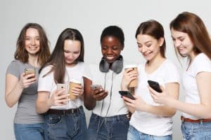 five different nation girls dressed in casual wear with smartphones