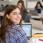 Close up face of school girl looking at camera while studying on computer.