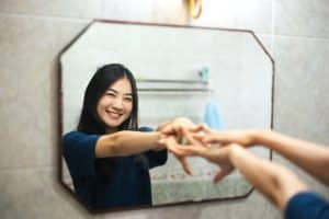 young asian woman looking at mirror looking happy