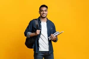 Smart arab guy student with backpack and bunch of books smiling at camera