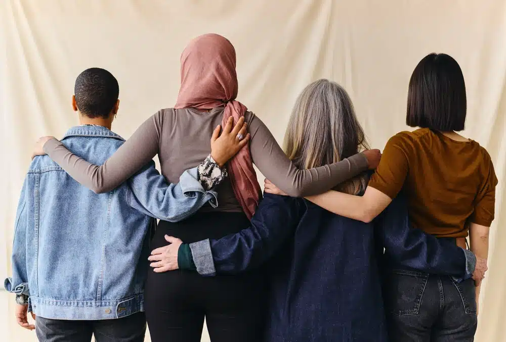 Rear view of four women with arms around each other in support of International Women's Day