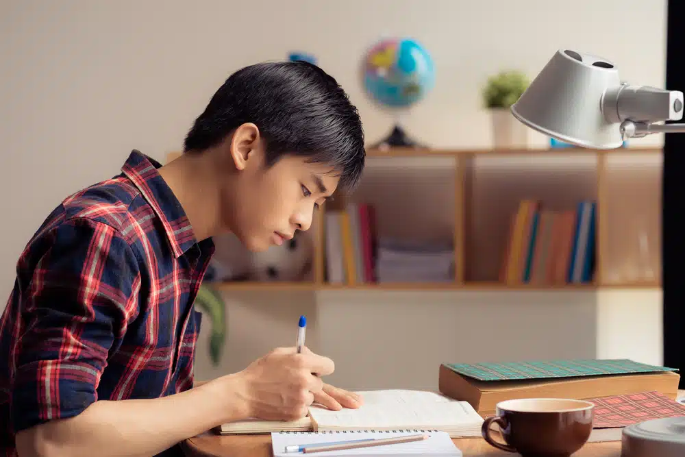 a male student writing an essay to his notebook