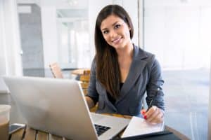 A woman smiling at the camera in front of her laptop.