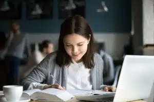 A student writing in a room in front of her laptop.