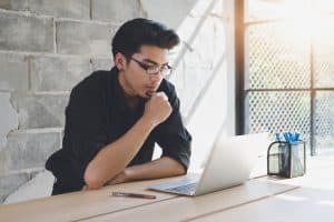 Male student using a laptop while sitting on a table.